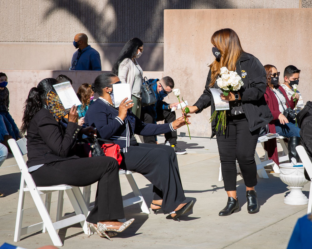 A woman hands out white roses to attendees of the Curtain of Courage Memorial Concept Unveiling