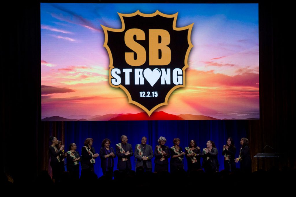 Members of a choir are onstage below an SB Strong image at the County Family Gathering
